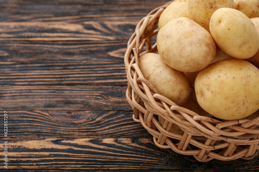 Wicker bowl with raw potatoes on wooden background