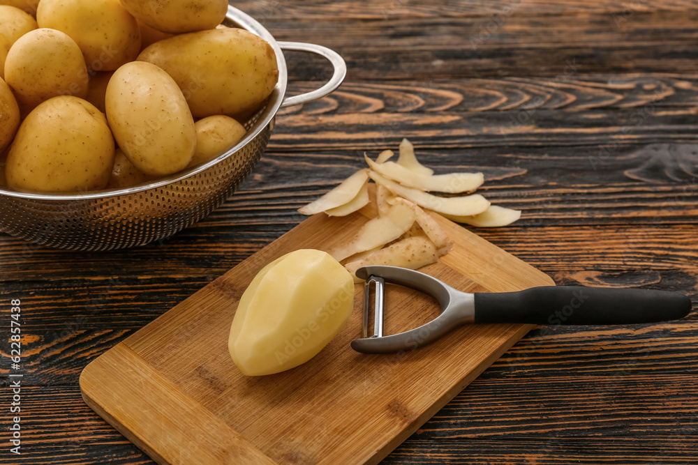 Board and colander with raw potatoes on wooden background