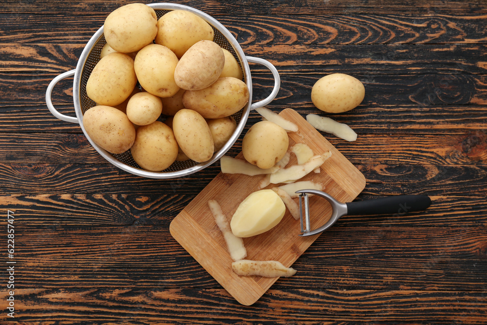 Board and colander with raw potatoes on wooden background