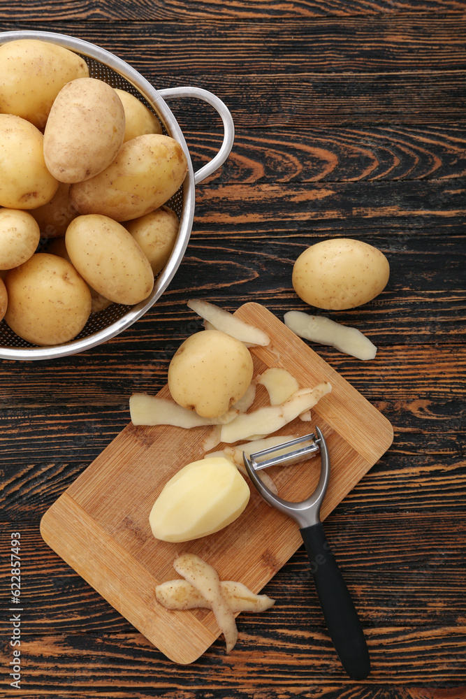 Board and colander with raw potatoes on wooden background