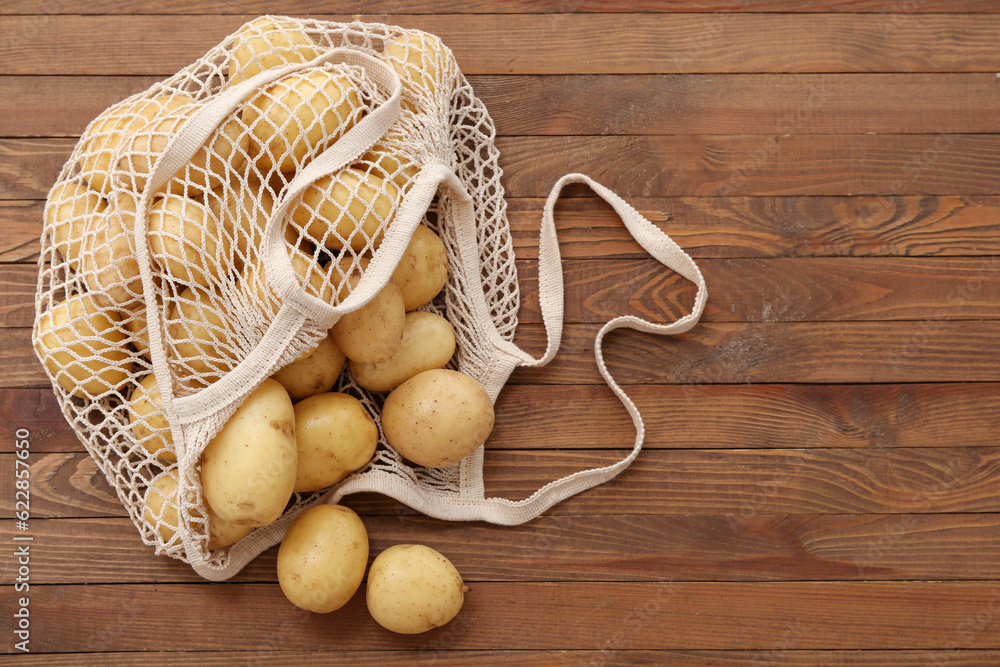 String bag with raw potatoes on wooden background