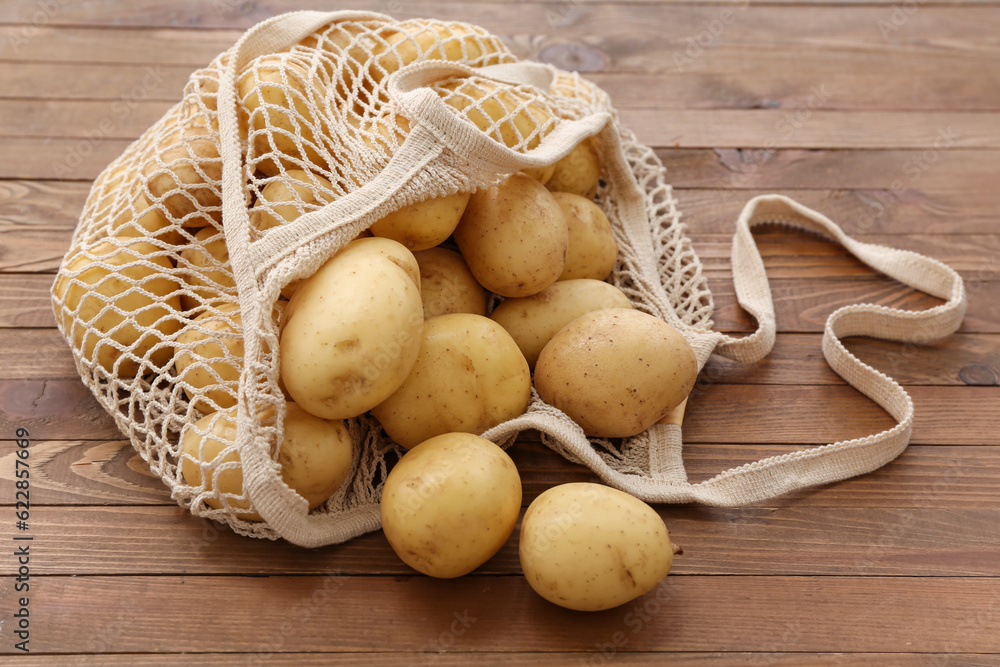 String bag with raw potatoes on wooden background