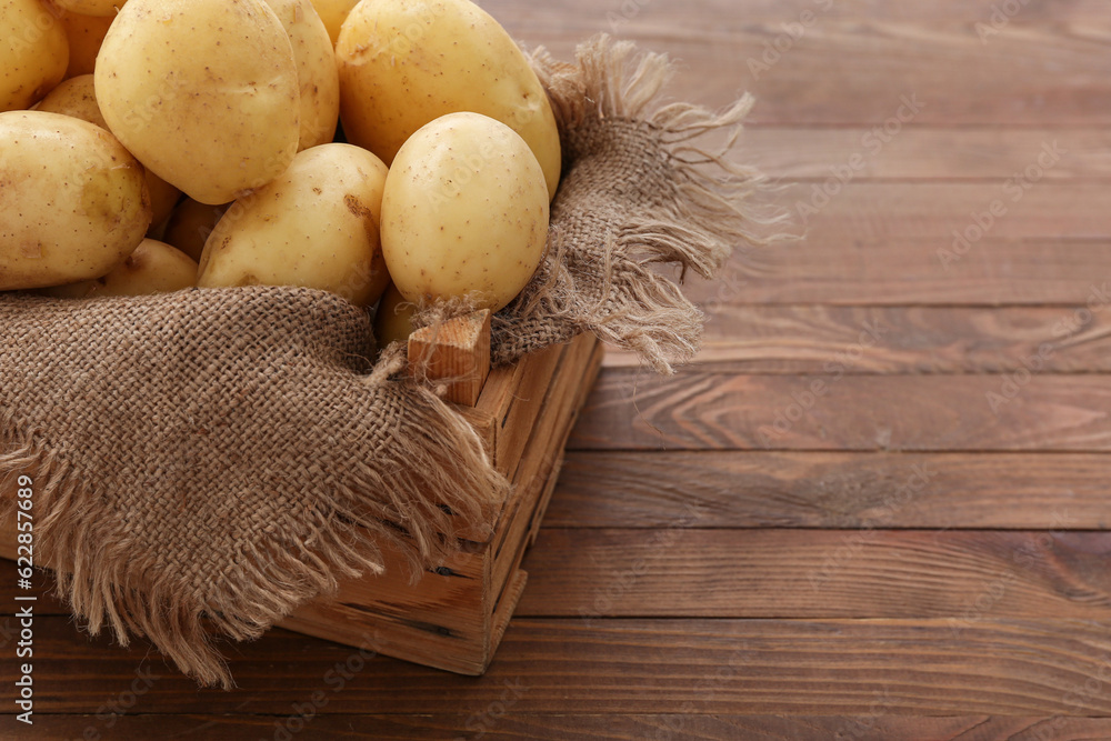 Box with raw potatoes on wooden background