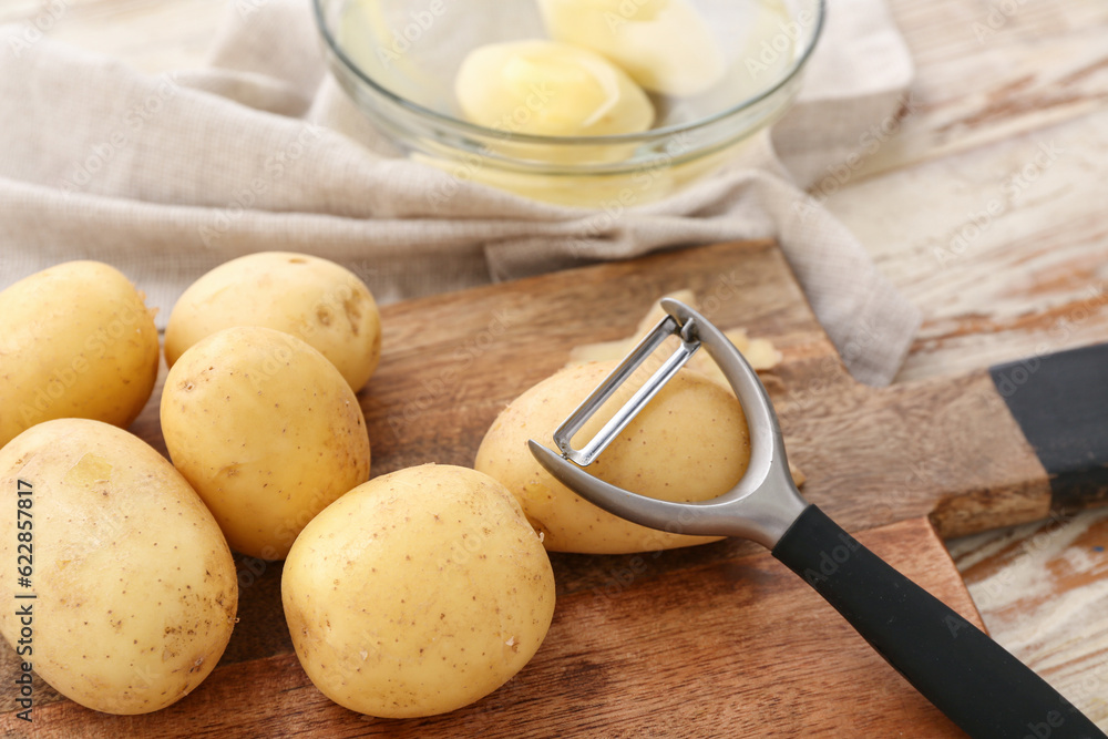 Board and bowl with raw potatoes on white wooden background