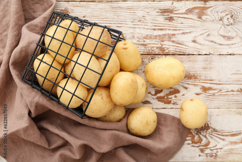 Basket with raw potatoes on white wooden background