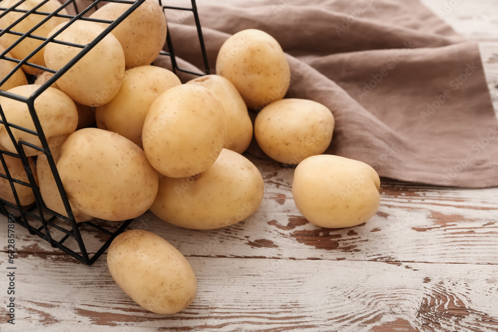 Basket with raw potatoes on white wooden background