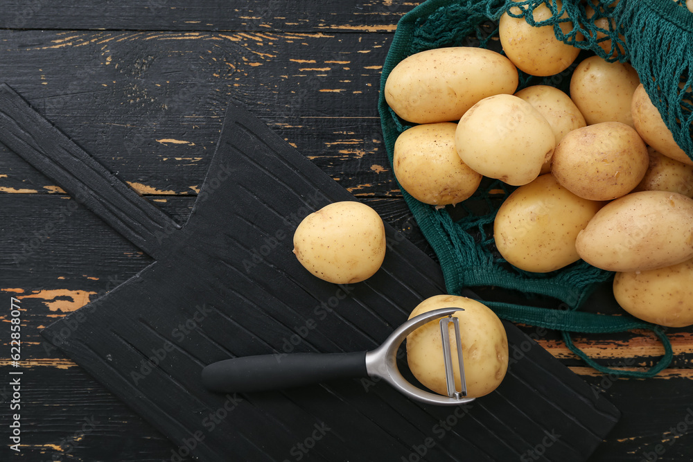 Board and string bag with raw potatoes on black wooden background