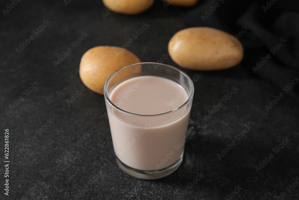 Glass of tasty potato milk on black background