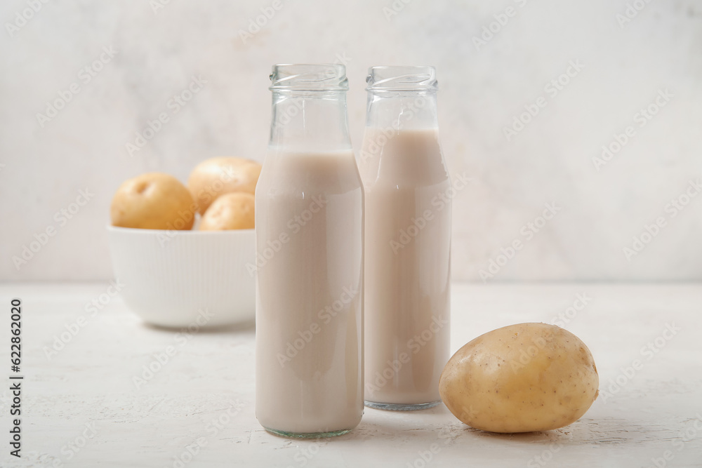 Bottles of tasty potato milk on light background