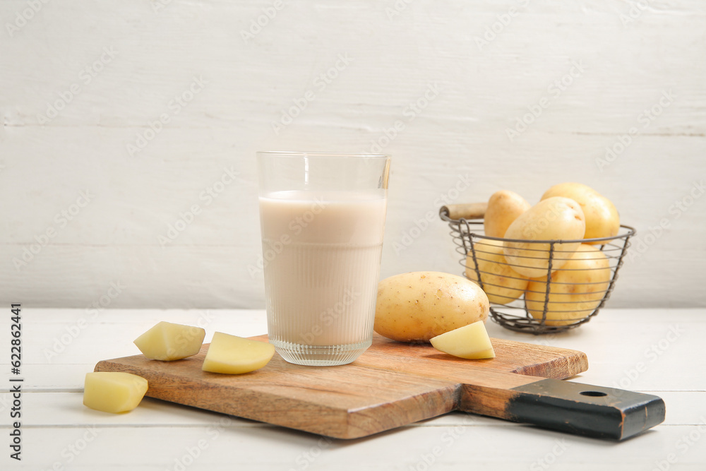 Glass of tasty potato milk on white wooden background