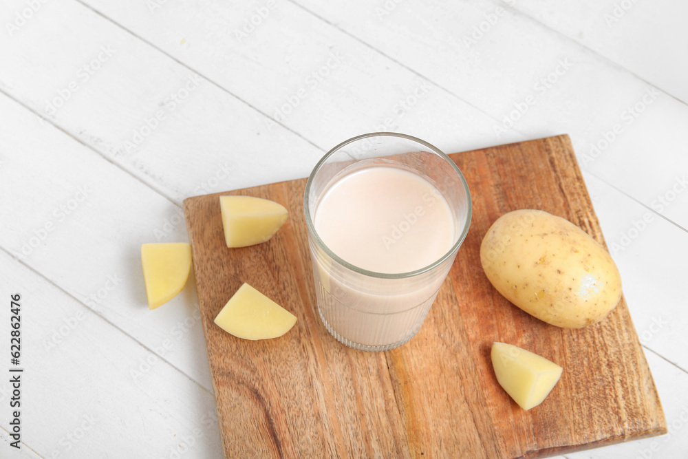 Glass of tasty potato milk on white wooden background