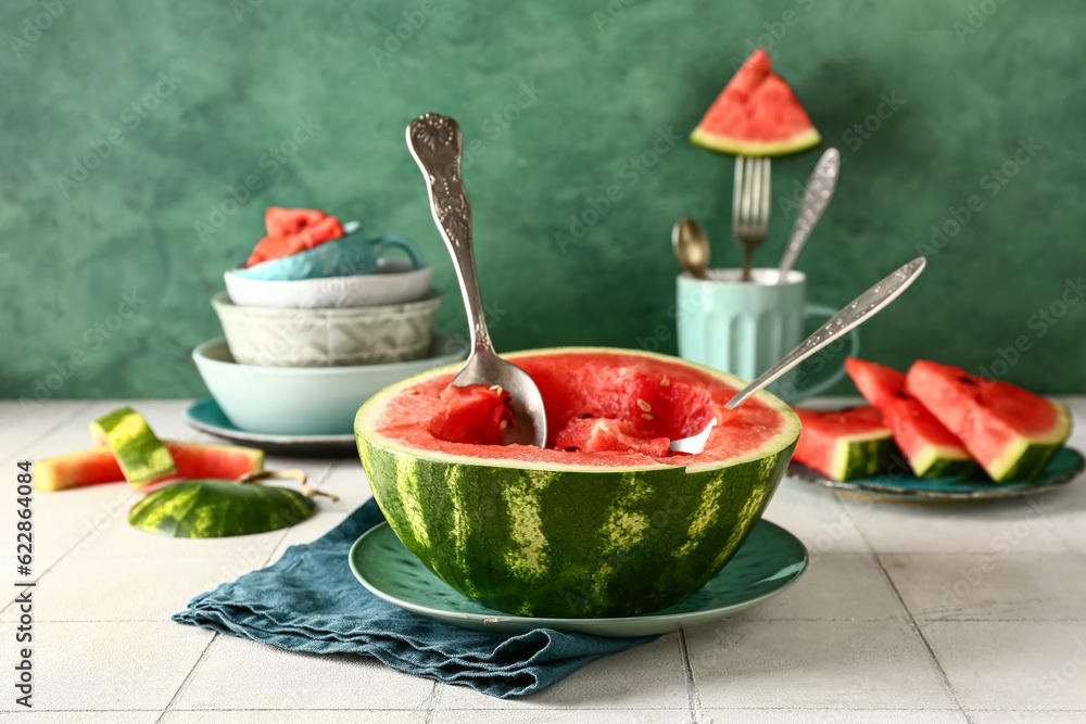 Plate with half of fresh watermelon and pieces on white tile table