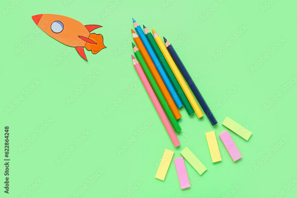 Pencils and stickers with paper rocket on green background