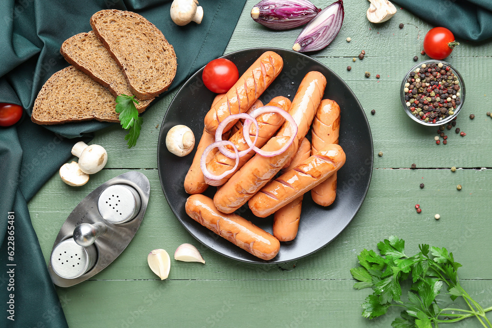 Plate with tasty sausages, bread and vegetables on green wooden table