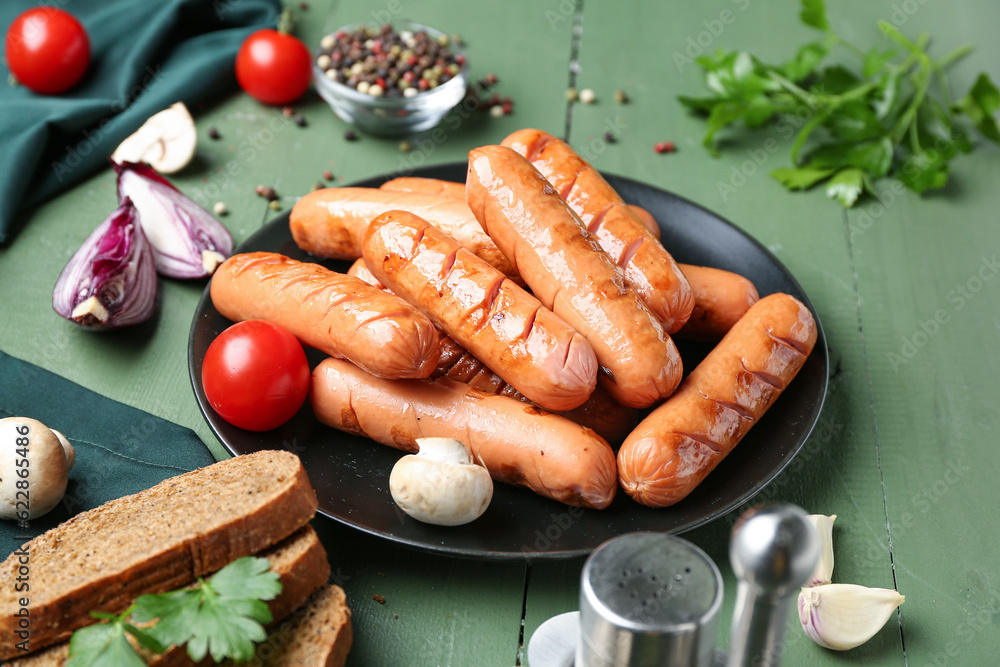 Plate with tasty grilled sausages and vegetables on green wooden table, closeup