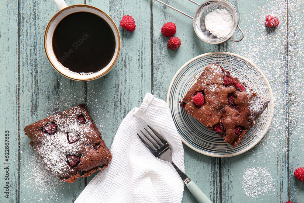 Plate with piece of raspberry chocolate brownie and cup of coffee on blue wooden table