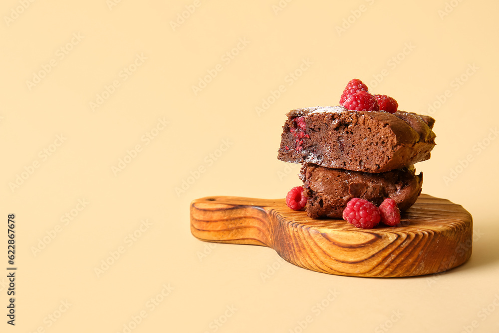 Wooden board with pieces of raspberry chocolate brownie on orange background