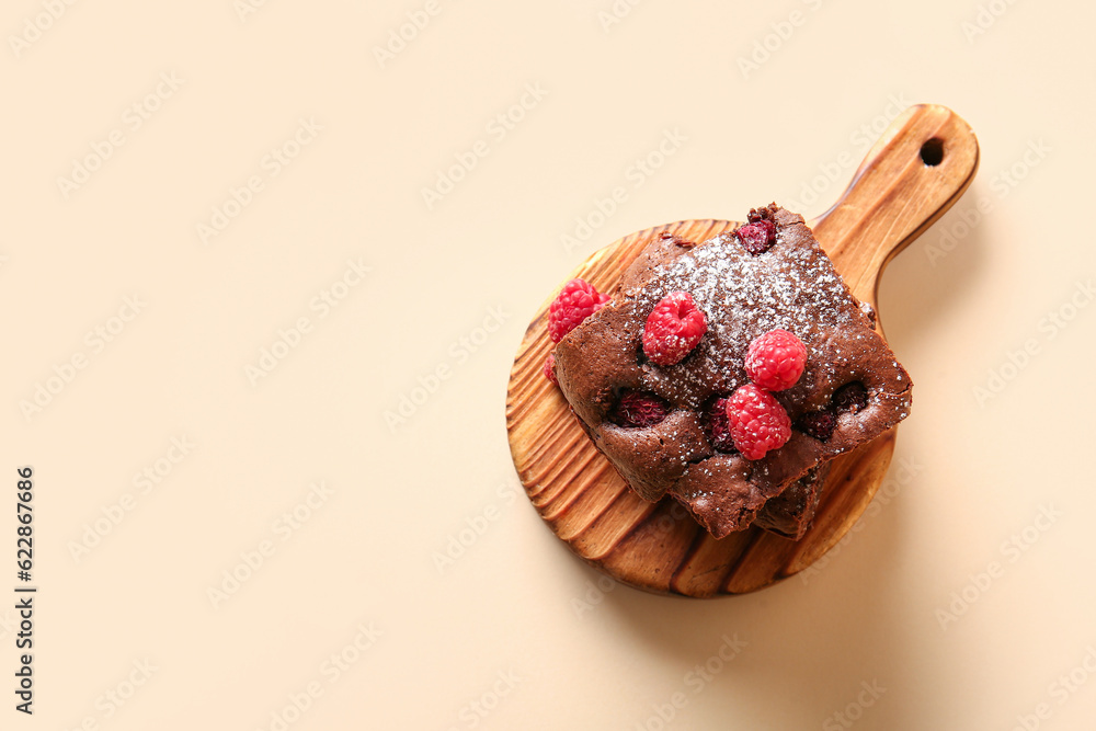 Wooden board with pieces of raspberry chocolate brownie on orange background