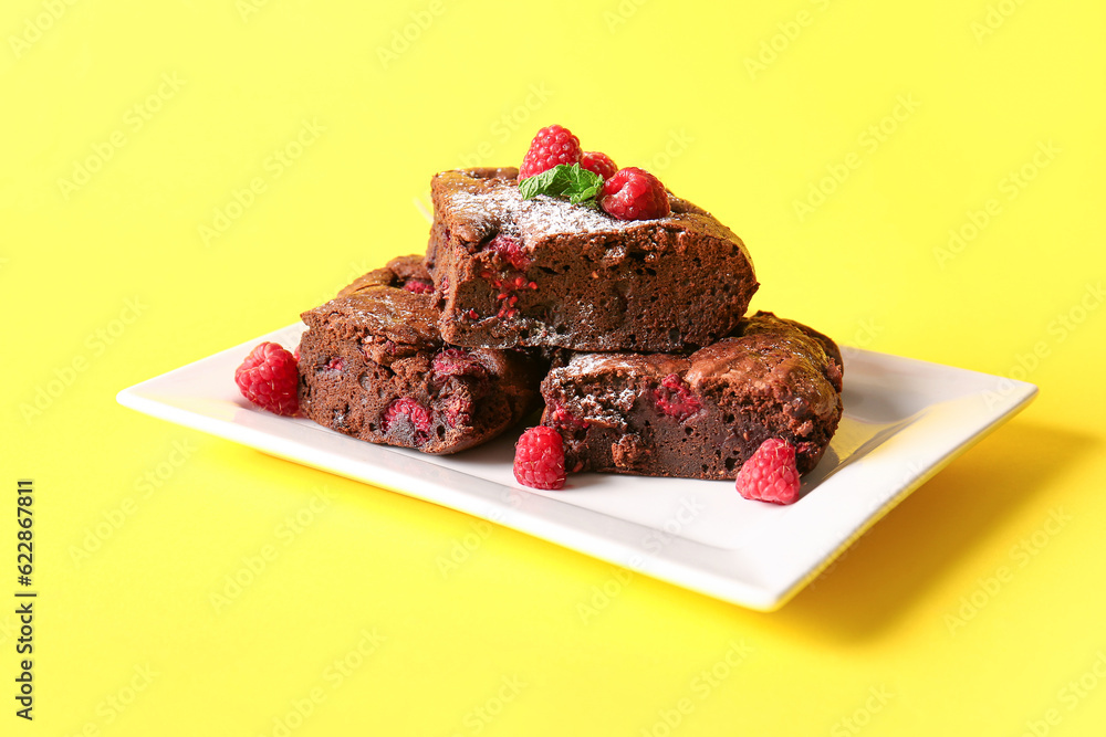 Plate with pieces of raspberry chocolate brownie on yellow background