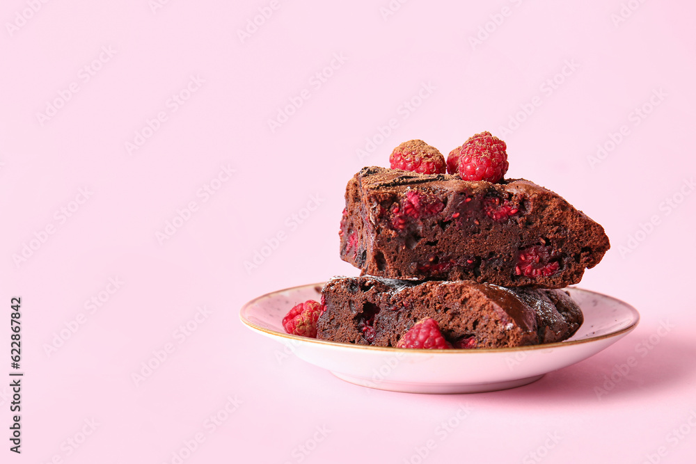 Plate with pieces of raspberry chocolate brownie on pink background