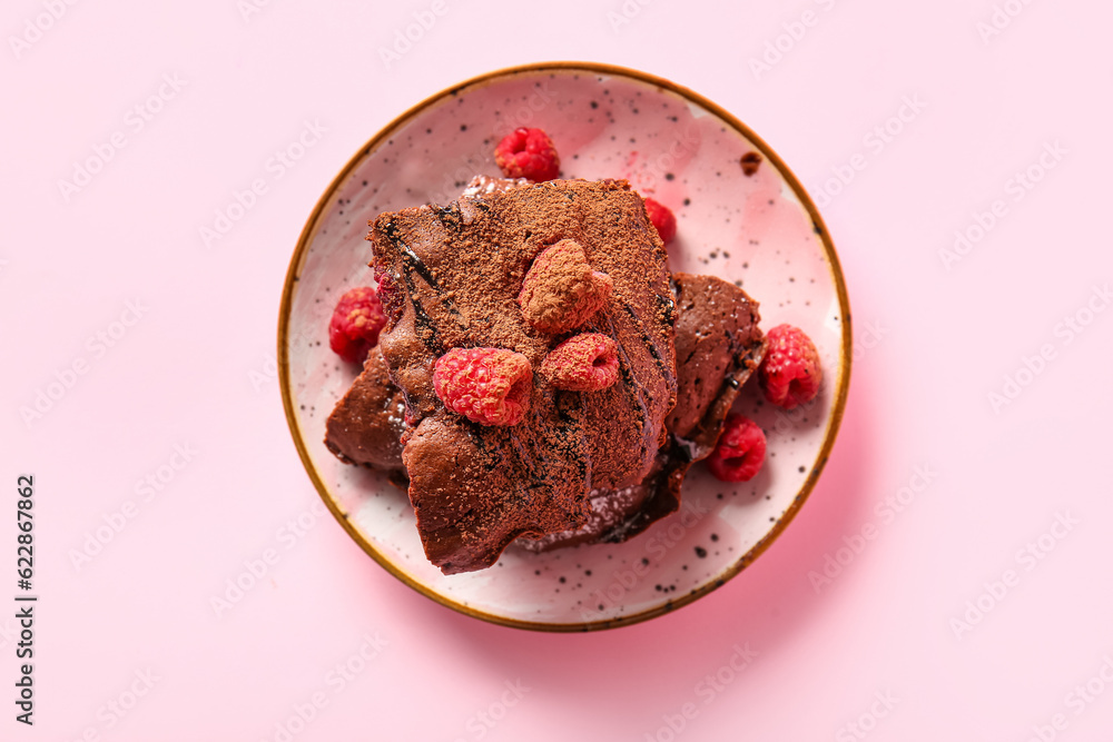 Plate with pieces of raspberry chocolate brownie on pink background