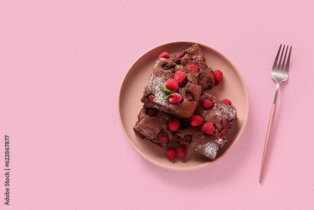 Plate with pieces of raspberry chocolate brownie on pink background