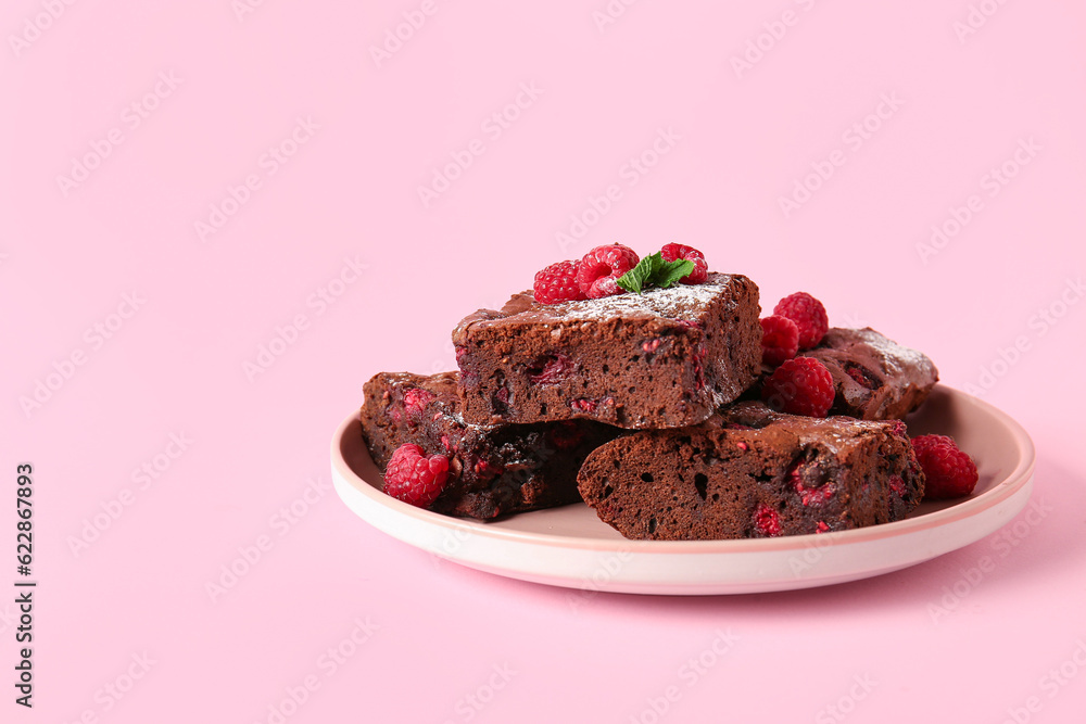 Plate with pieces of raspberry chocolate brownie on pink background