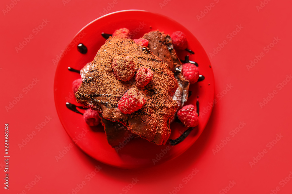 Plate with pieces of raspberry chocolate brownie on red background