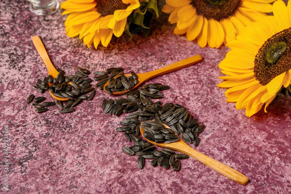 Sunflowers and spoons with seeds on purple background