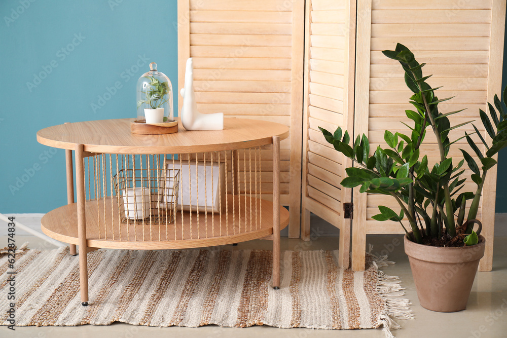 Coffee table with decor, houseplant and folding screen near blue wall