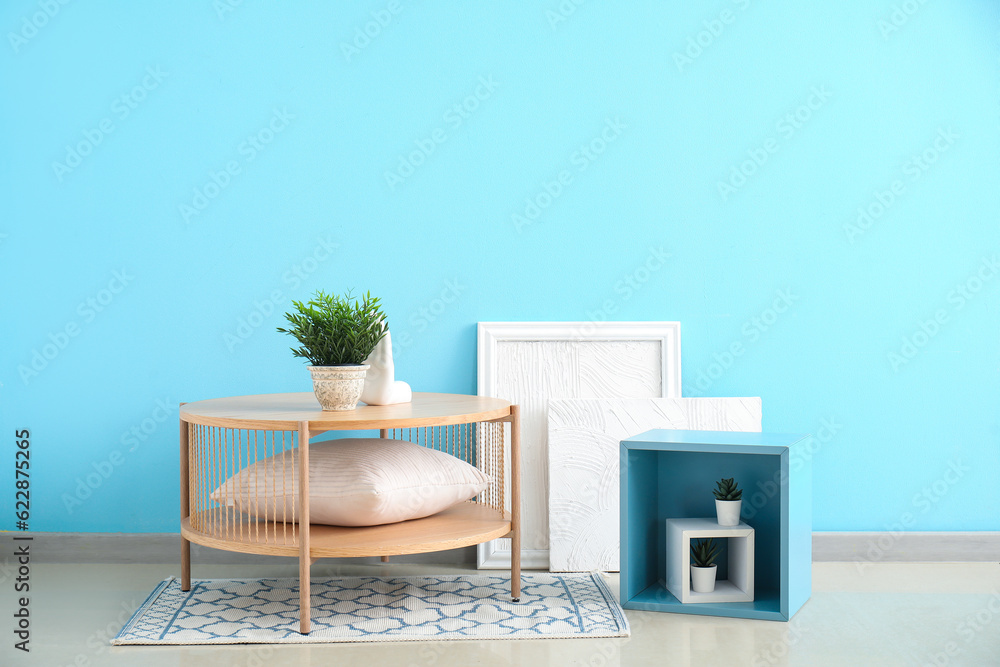 Coffee table with houseplant, cushion and decor near blue wall