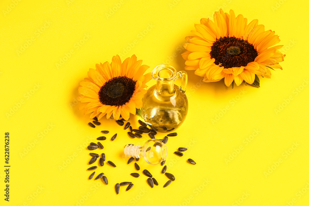 Sunflowers, seeds and decanter of oil on yellow background