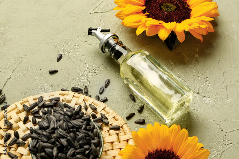 Sunflowers, seeds and bottle of oil on green background