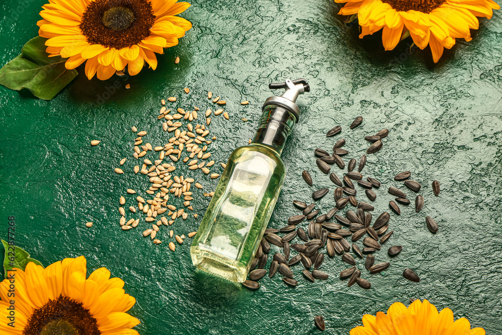 Sunflowers, seeds and bottle of oil on green background