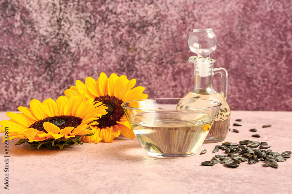 Sunflowers, seeds, bowl and decanter of oil on pink background