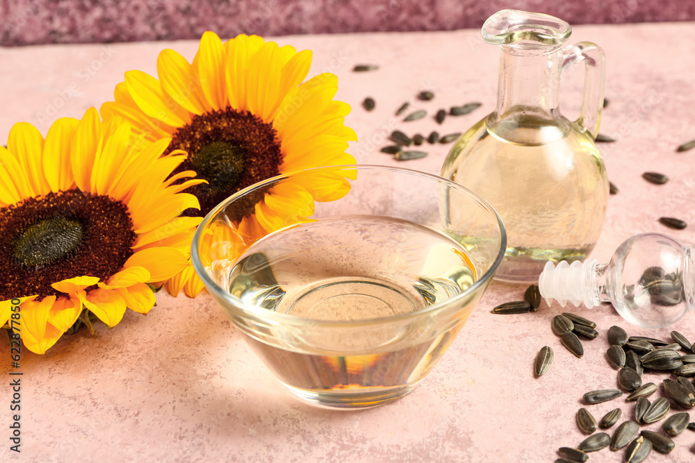 Sunflowers, seeds, bowl and decanter of oil on pink background