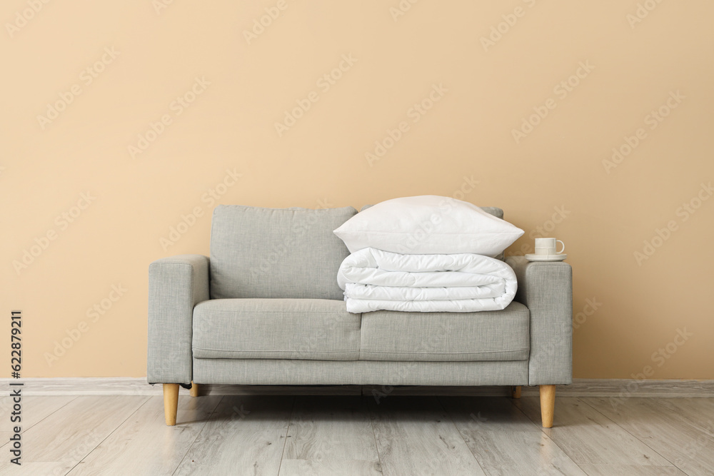 Grey sofa with folded white blanket and pillow near beige wall