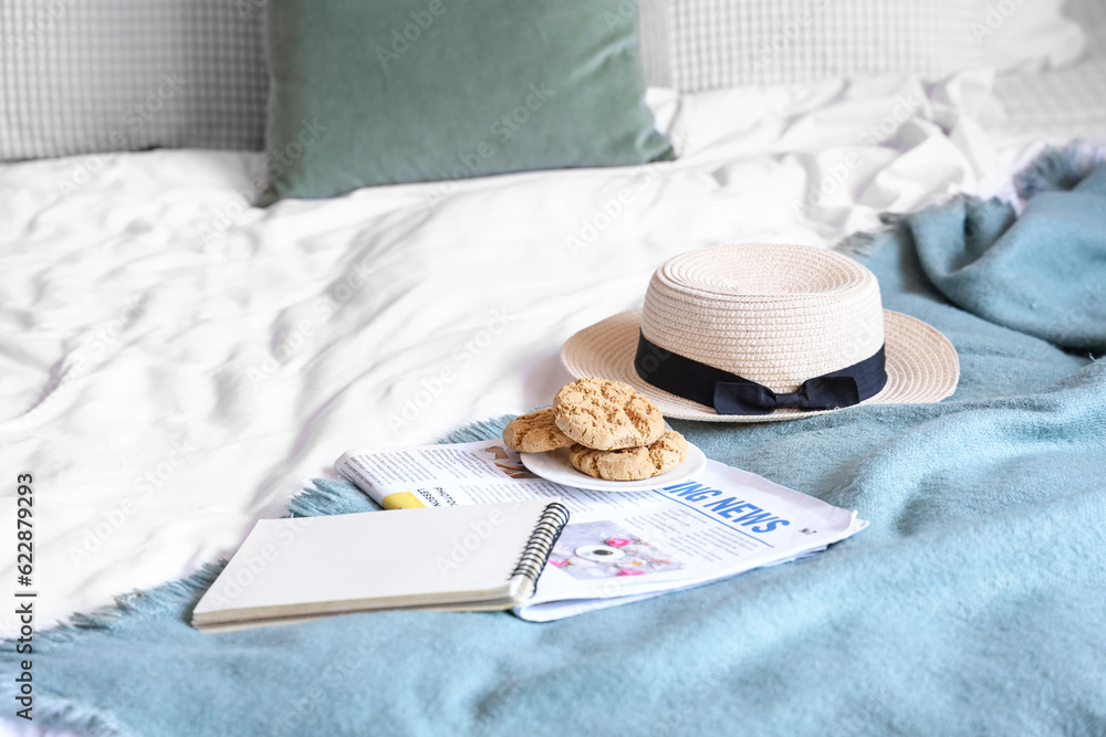 Cookies, newspaper and hat on cozy bed in bedroom