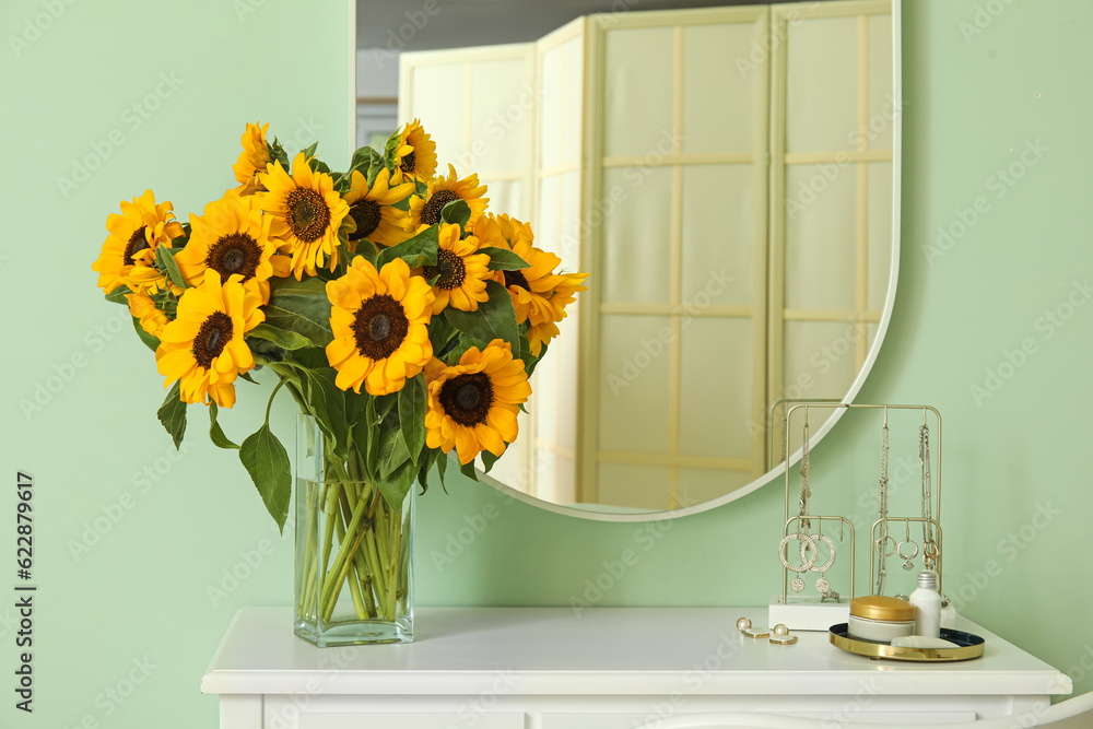 Vase with beautiful sunflowers on dressing table near green wall