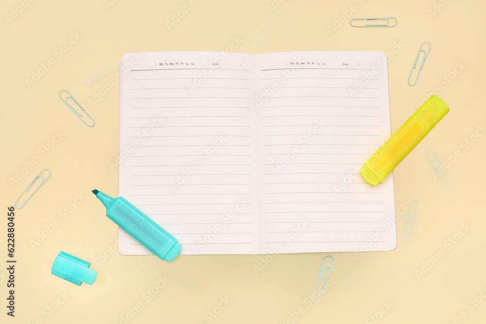 Blank notebook with stationery on pale yellow background