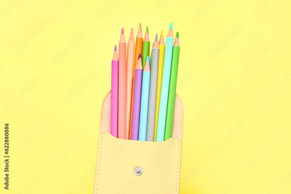 Different colorful pencils in case on yellow background