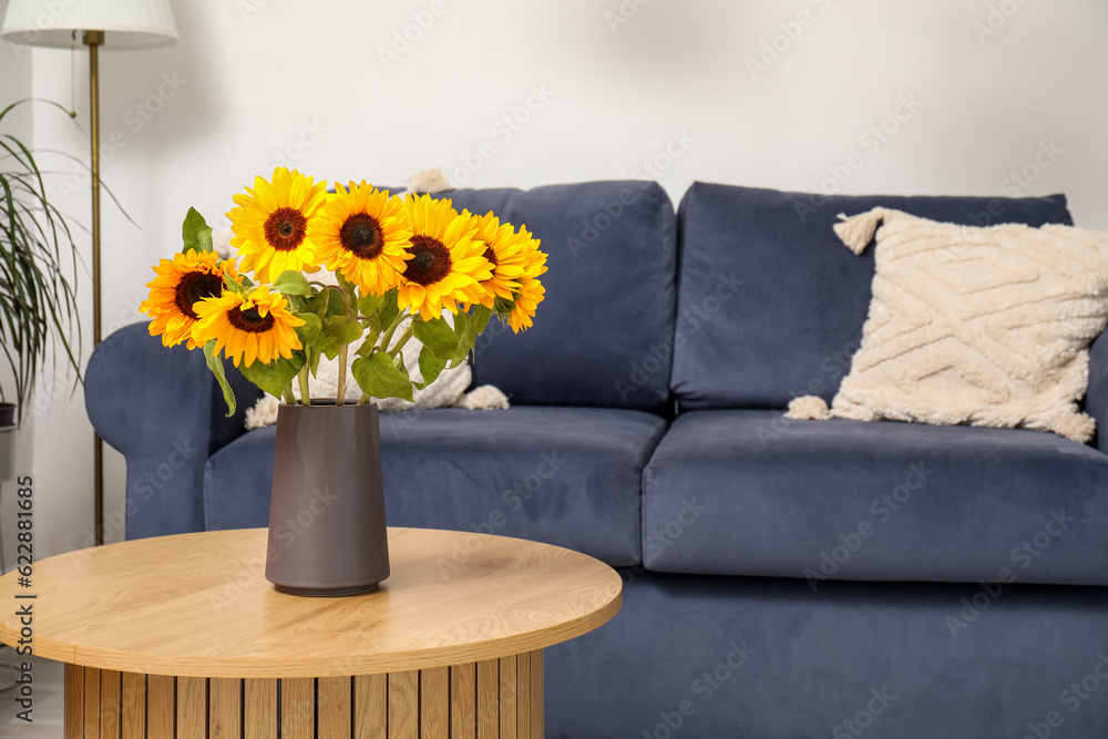 Blue sofa and vase with beautiful sunflowers on wooden coffee table in living room