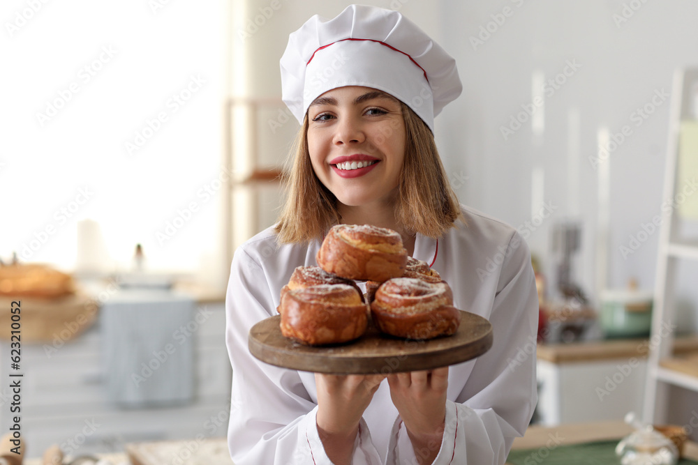 Female baker with board of tasty buns in kitchen, closeup