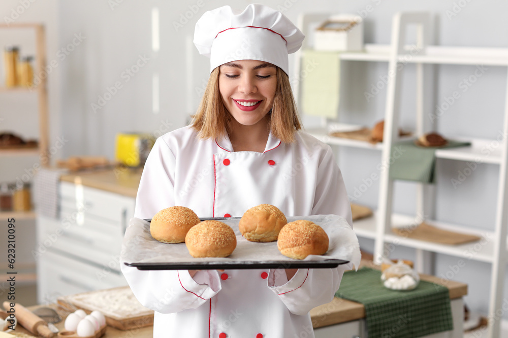 Female baker with tray of tasty buns in kitchen