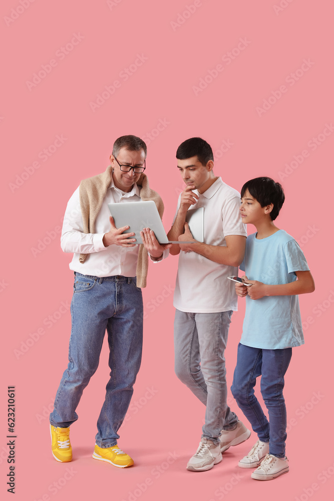 Happy little boy with his dad and grandfather using laptop on pink background