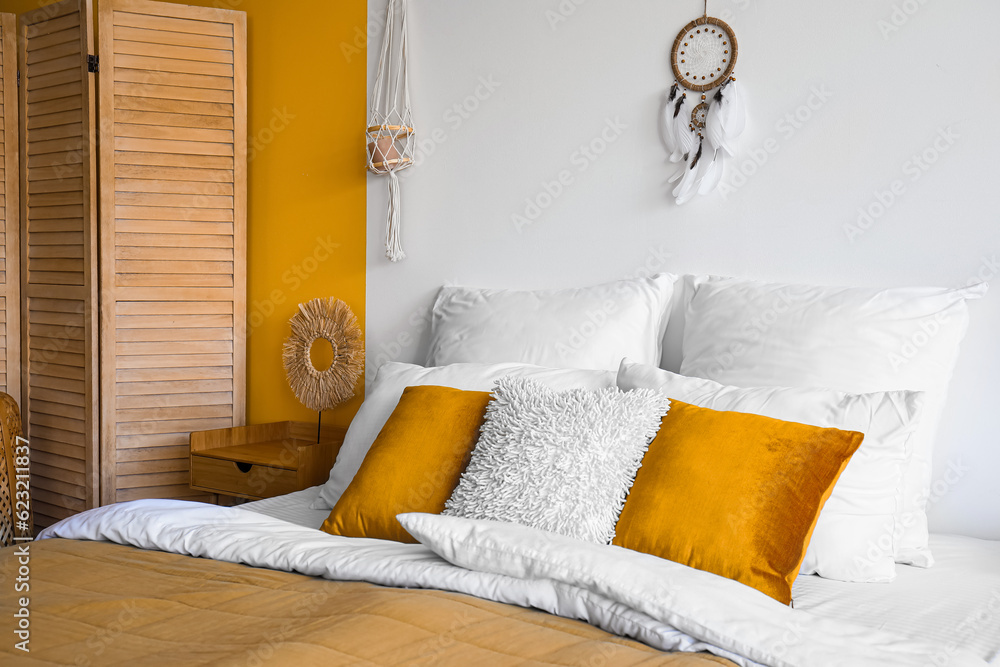 Interior of modern bedroom with bed, wooden folding screen and dream catcher hanging on white wall