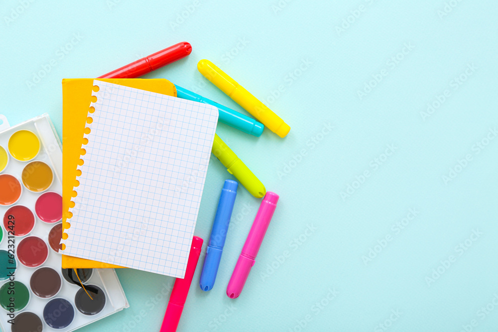 Blank notebook with different colorful markers and paints on blue background