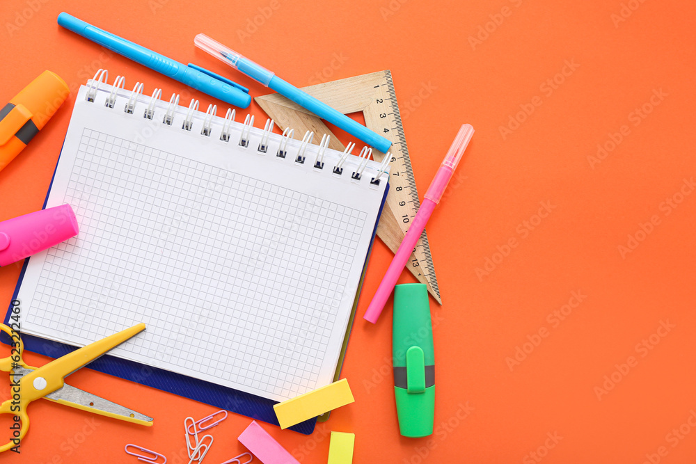 Blank notebook with different stationery on orange background