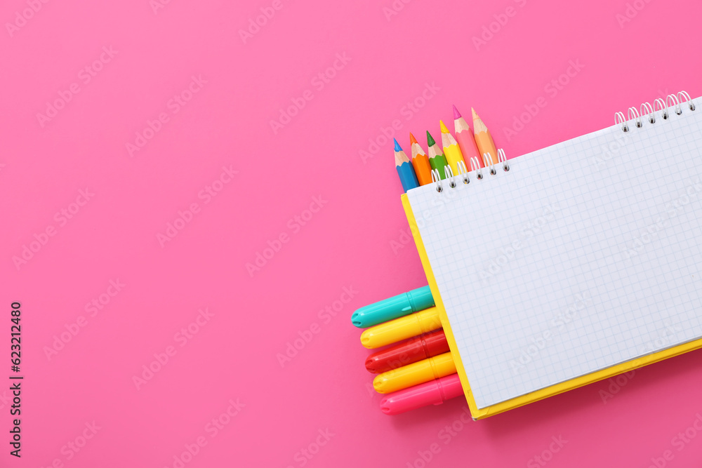 Blank notebook with different colorful markers and pencils on pink background