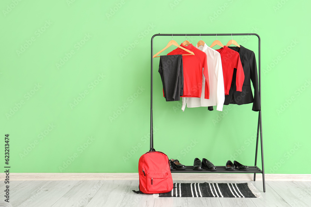 Stylish school uniform hanging on rack, backpack and shoes near green wall in room